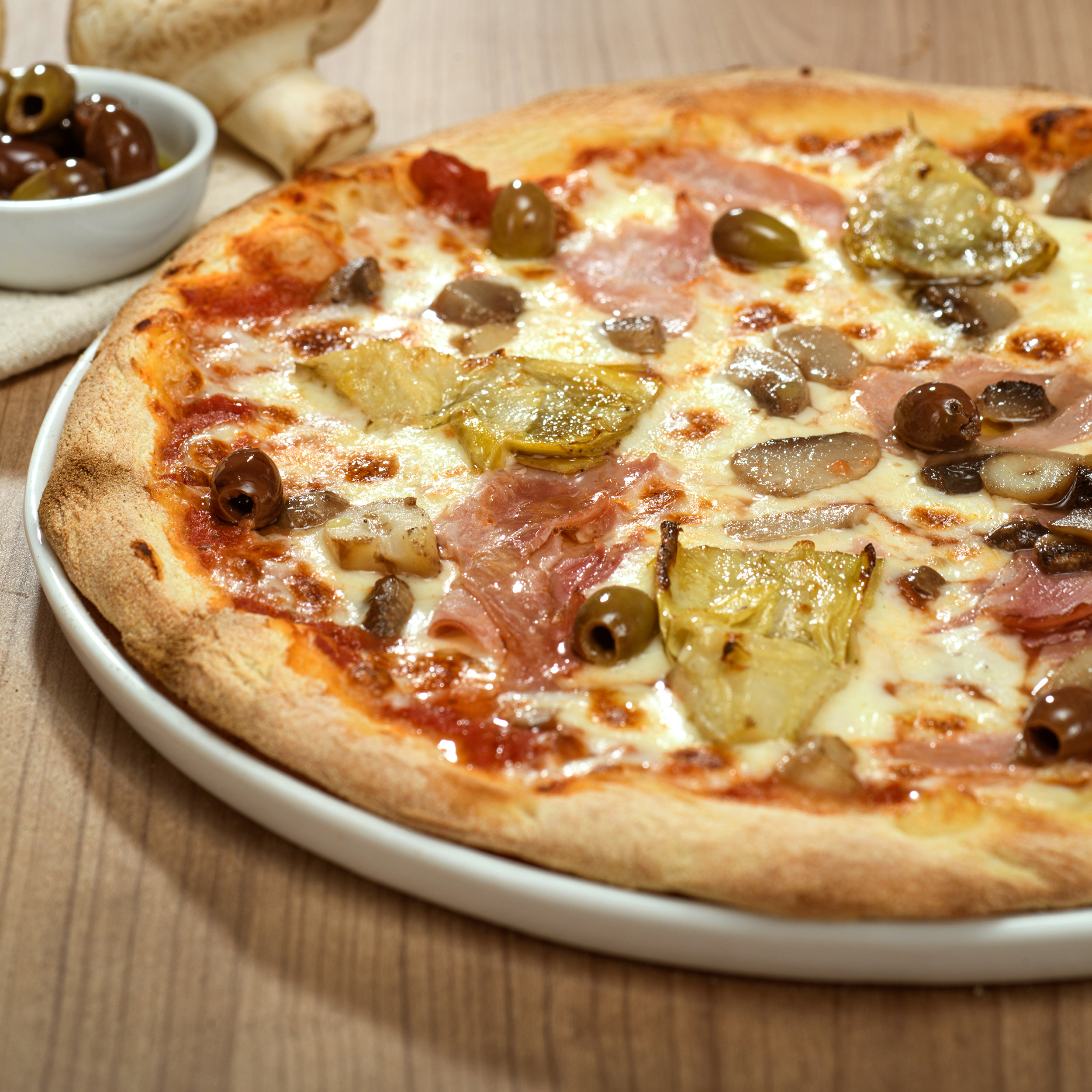 Pizza Capricciosa avec sauce tomate, mozzarella Fior di Latte, jambon, champignons, cœurs d’artichauts et olives – pizza italienne à emporter ou en livraison